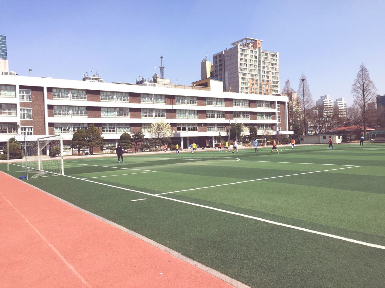 building exterior, architecture, built structure, clear sky, city, grass, lawn, incidental people, building, city life, day, sunlight, outdoors, green color, blue, residential building, facade, residential structure, travel destinations, sky