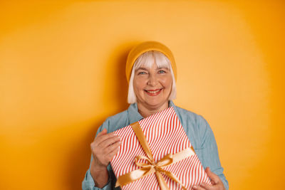 Portrait of young woman standing against yellow background