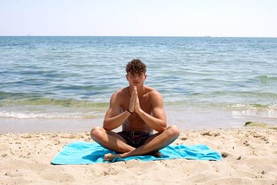 Young woman sitting on shore at beach against sky