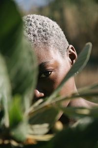 Serious african american female with short dyed hair covering face with branch and gazing at camera
