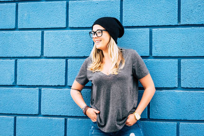 Full length of a smiling young woman standing against wall