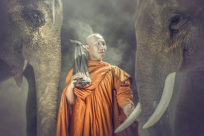 Monk standing amidst elephants