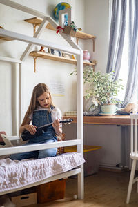 Cute girl playing ukulele at home