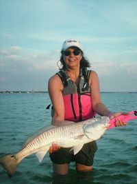 Portrait of woman holding fish while standing in sea