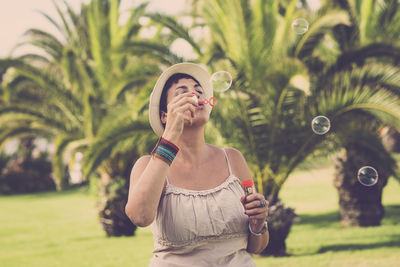 Woman wearing hat playing with bubble wand against plants