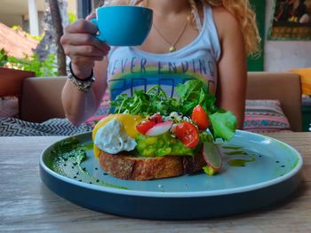 Midsection of woman holding coffee cup over food in plate