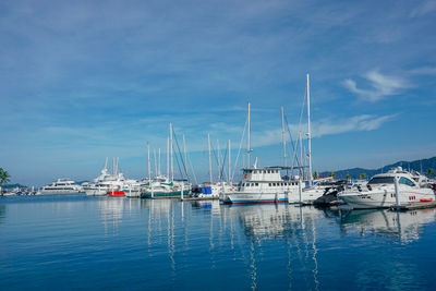 Sailboats moored at harbor against blue sky