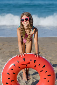 A girl in a swimsuit plays with an inflatable ring on the beach. vertical shot.