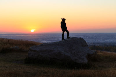 Silhouette of young boy standing on a rock in a park at sunrise
