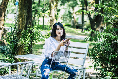 Young woman sitting on chair against plants