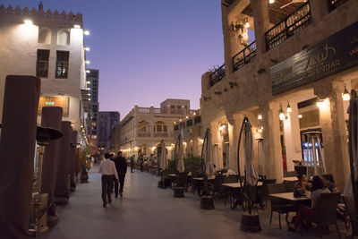 People on illuminated street amidst buildings in city at dusk