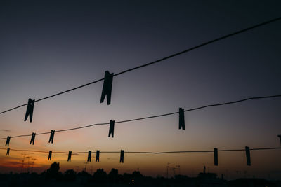 Silhouette clothespins hanging on clotheslines against sky during sunset