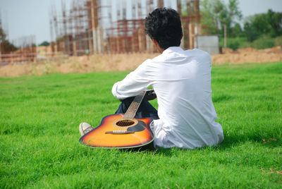 Rear view of man sitting with guitar on grass