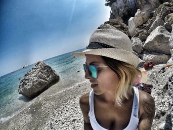 Young woman wearing sunglasses on rock at beach