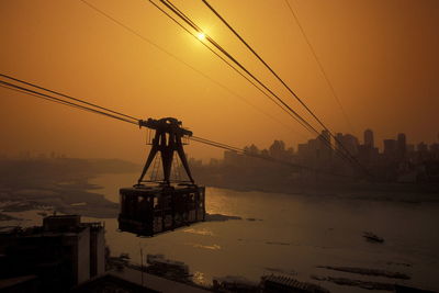 Overhead cable car above river against sky during sunset