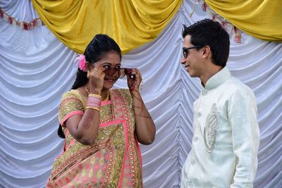 Young couple wearing sunglasses while standing against curtain