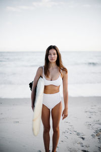 Portrait of young bikini woman with surfboard standing at beach