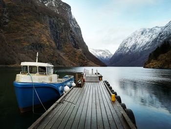 Boats moored on pier by lake against sky