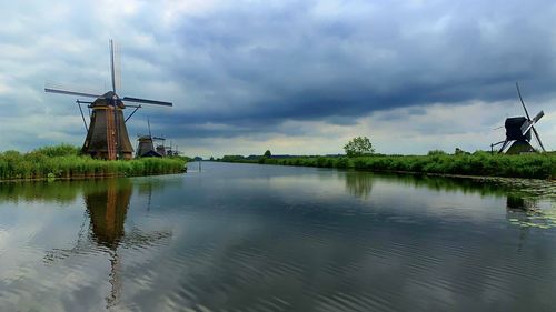 Traditional windmill by lake against sky