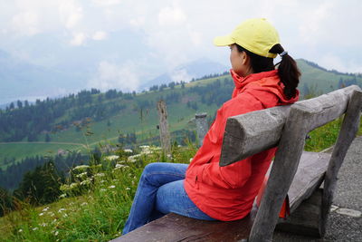 Side view of mature woman looking at landscape while sitting on bench against sky