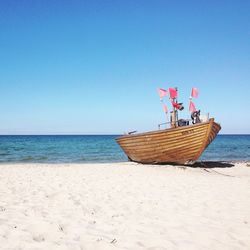 Boat moored on beach by sea against clear sky