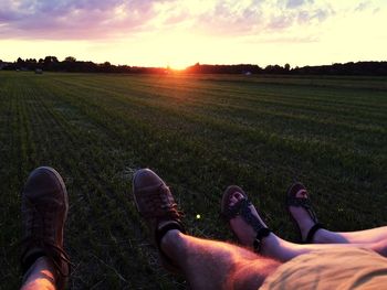 Low section of people on field against sky during sunset