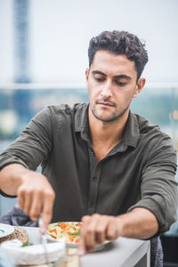 Young man cutting mozzarella at building terrace during party