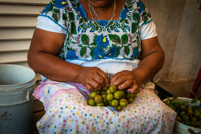 Midsection of woman holding limes while sitting against wall