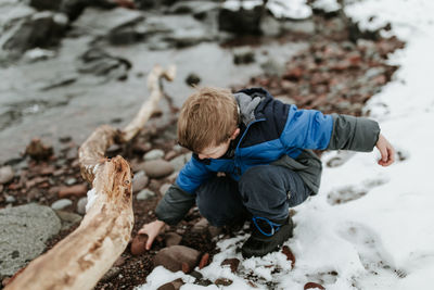 Boy playing with rock on lakeshore during winter
