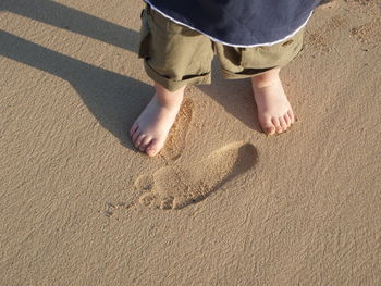 Low section of boy standing in front of footprint on sandy beach