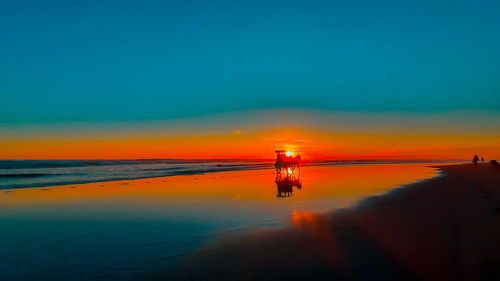 A silhouetted horse-drawn carriage at sunset time on the wet and reflecting sand beach in indonesia.