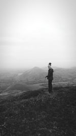 Female hiker standing on field at mountain against sky during winter