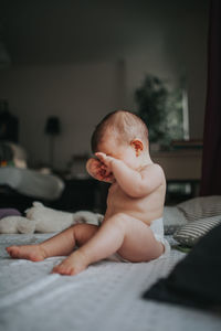 Full length of shirtless baby girl sitting on bed at home