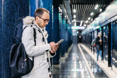 Adult man with wait train at the subway station. male write message or read news on smartphone.