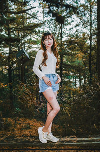 Portrait of young woman standing against trees in forest