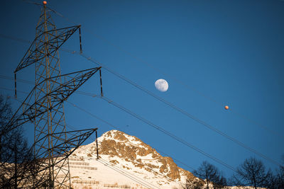 Low angle view of electricity pylon against clear blue sky