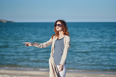 Woman gesturing while standing by sea against sky