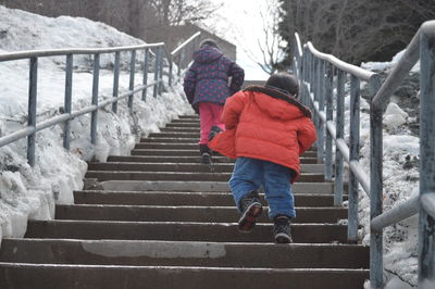 Low angle view of siblings walking up on steps amidst snowy field