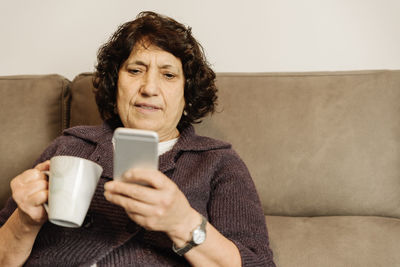 Mid adult man holding coffee cup on sofa at home