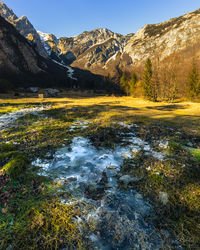 Scenic view of stream flowing by mountains against sky