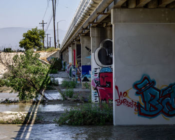 Graffiti on building by river against sky