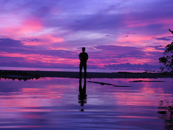 Silhouette man standing on lake against sky during sunset
