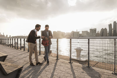 Usa, new york city, two young men walking along east river looking at cell phone