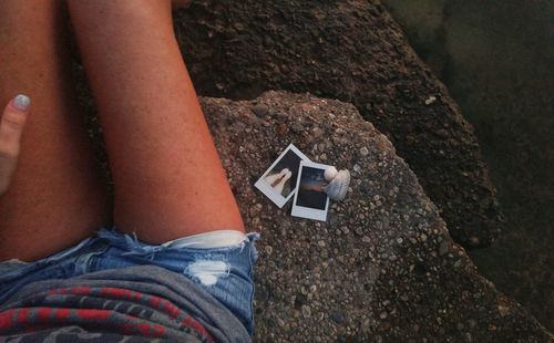 Midsection of young woman sitting with photographs on rocks