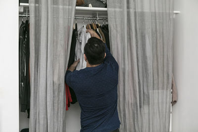 Rear view of man hanging clothes in closet at bedroom