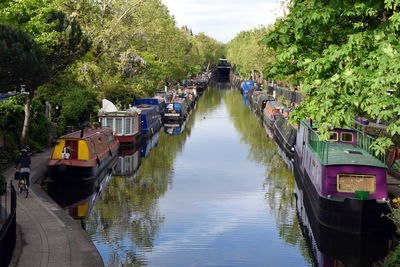 Boats moored in river by trees against sky