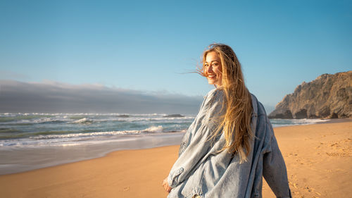 Rear view of woman standing at beach against sky