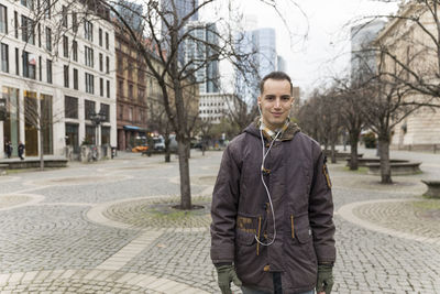 Portrait of smiling man listening music while standing in city