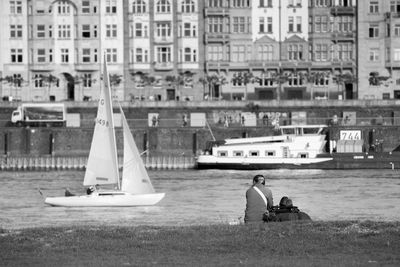 Rear view of people at riverbank against buildings in city