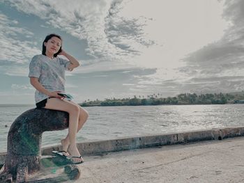 Full length of woman sitting on metal against sea